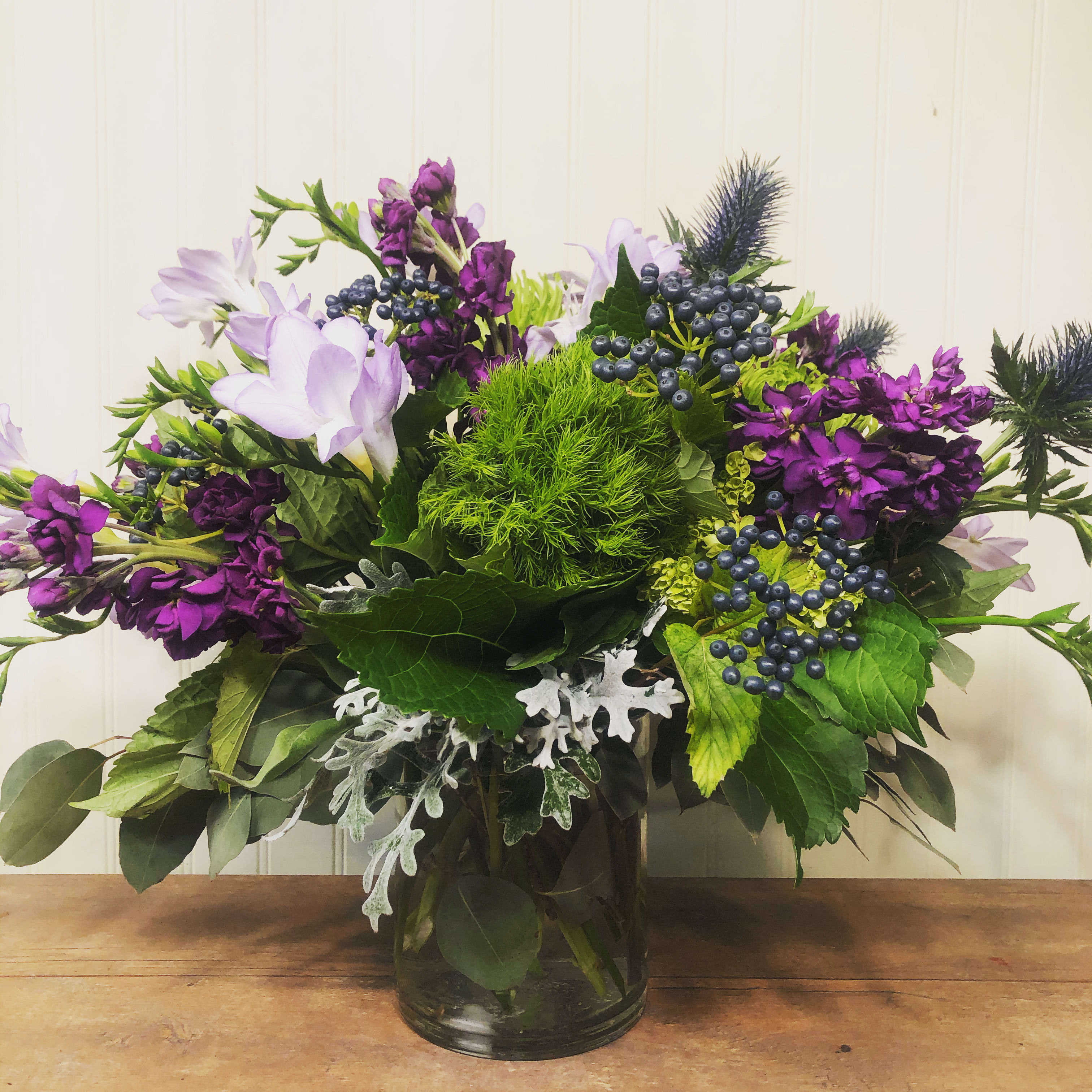 Jack and Dusty Vase Arrangement Jack and Dusty Vase Arrangement - Sweet smelling purple stock and freesia combined with fuzzy textured green trick dianthus and thistle. Finally, accented with Black Jack Vibernum Berry and Dusty Miller in a clear glass cylinder. This creation is complicated and so exciting at the very same time. All of the senses are affected here, it's visually stunning, texturally stimulating and aromatically intoxicating. Give it a try, you won't regret it. Approx. Size 12" x 10" *Due to availability, on occasion it may be necessary to substitute a certain flower or container for your order.
