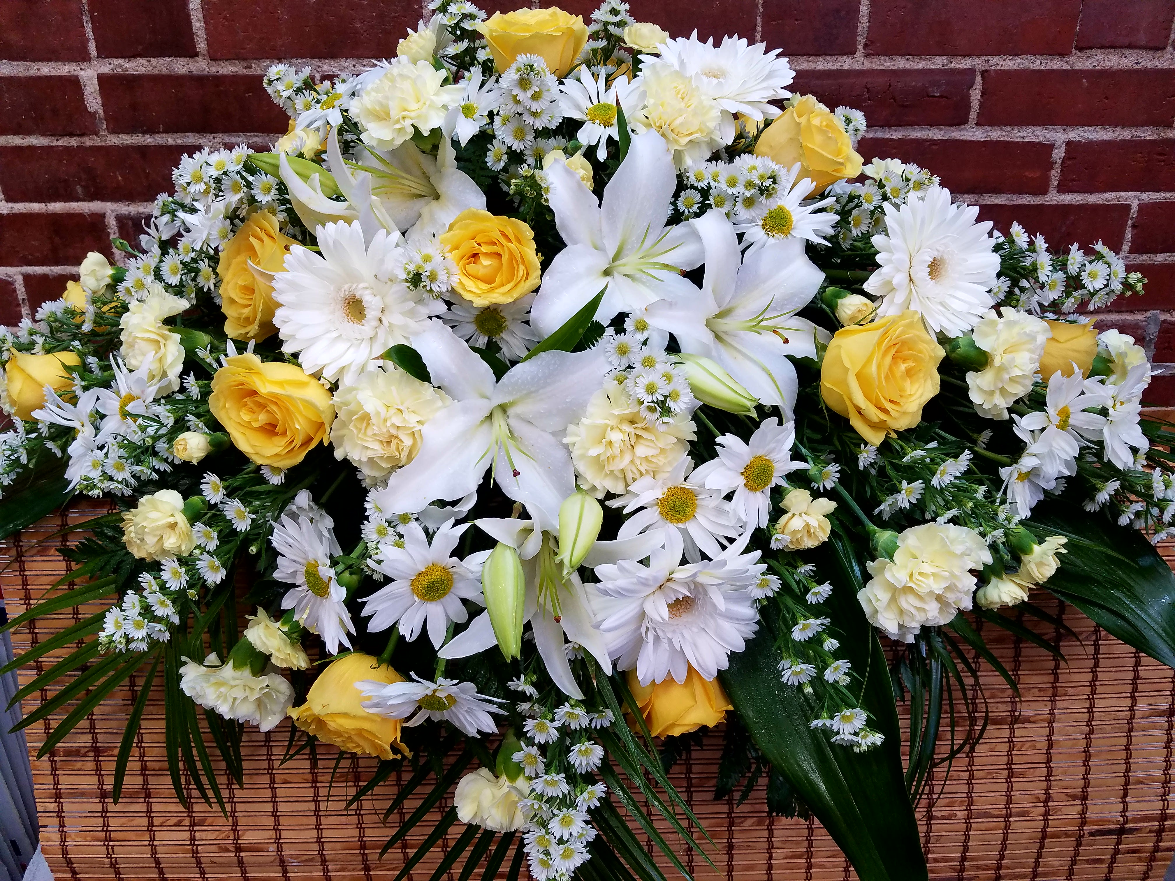 Eckert Florist's Yellow And White Casket Spray - This casket adornment features our finest yellow and white flowers available. Flowers may include white lilies, white gerbera daisies, white chrysanthemum daisies, yellow roses and yellow carnations. Filler flower and foliage will also be added.  