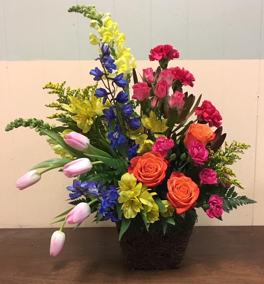 Colorful Elegance - A rainbow of colors gleams from this beautiful basket. Orange roses, pink spray roses, yellow alstromaria, pink carnations, hot pink mini carnations, blue delphinium, yellow solidago, yellow snaps, pink tulips are surrounded by multiple greens to make this a stylish gift for that special someone!