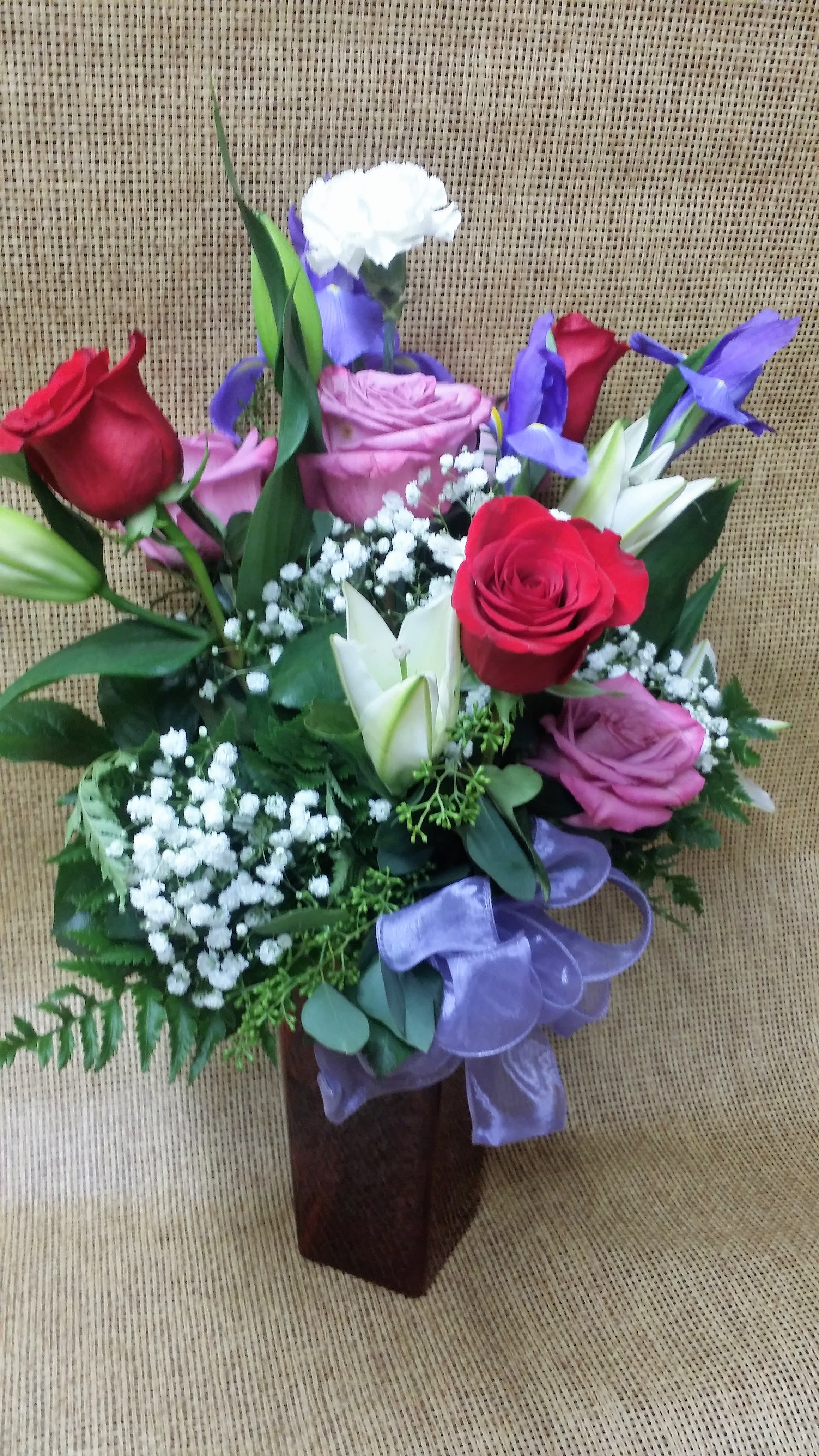 Spring Palette - Mixed roses, blue Asian iris and white lilies, accented by sprigs of baby's breath and seeded eucalyptus, make for a lovely spring bouquet. Comes in a red square vase.