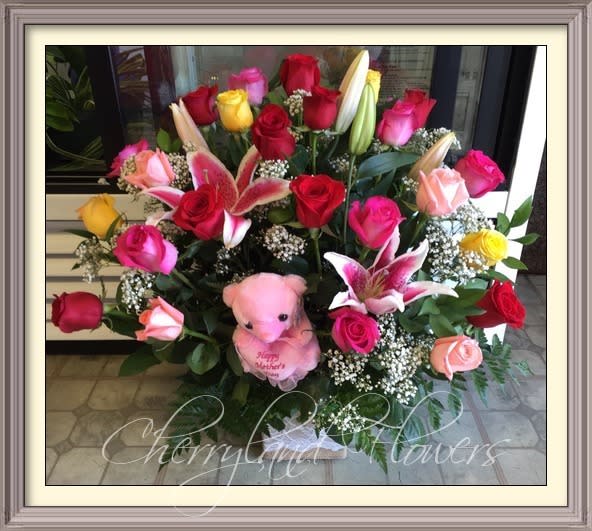 CF1088 - Celebrate Mother's Day with this unique floral masterpiece featuring a lush combination of fresh multicolored roses, pink stargazers, baby's breath, and foliage adorned with a petite Mother's Day bear in the center. 