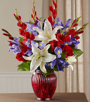 CF2077 - Loyal Heart  Celebrate a life dedicated to the love of country with a vibrant bouquet of red, white and blue blossoms beautifully hand-arranged. This bright and beautiful tribute evokes loving memories of the deceased's devotion to the nation−in the armed forces, as a government worker or as a public spirited patriot. Its red roses, white gladiolus and Oriental lilies, and blue irises beautifully reflect the colors of their beloved flag and are arranged in a classic vase of ruby red glass. It is sure to be long remembered at a wake, funeral service or for offering your condolences at the home of grieving family and friends.