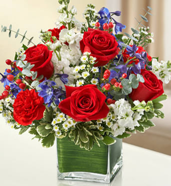 CF2079 - Healing Tears  This lovely red, white and blue sympathy arrangement offers a beautiful reflection of your patriotism, sympathy and support. Fresh red roses, delphinium, stock, carnations and hypericum, designed in a cube vase, provide a stunning tribute sent to the home or service.
