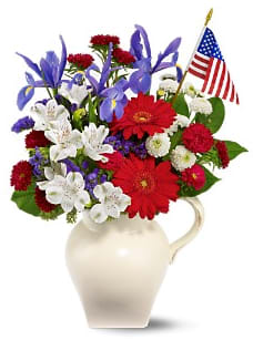 CF2090 - Patriotic Pitcher  Honor the hope and spirit of America with a red, white and blue bouquet of perfectly fresh flowers… presented in a classic ivory pitcher, and topped off with the Stars &amp; Stripes! This lovely bouquet will be received with gratitude, and displayed with pride. Details: Red gerberas and Matsumoto asters, white button spray chrysanthemums and alstroemeria and blue iris – accented with sinuata statice, seeded eucalyptus and salal – are delivered in an ivory handled pitcher with an American flag. 