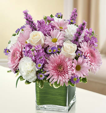 BN 95420 - Healing Tears - Lavender and White Let the comforting beauty of elegant lavender and white blooms send a caring message of your sympathies. Lovely roses, stock, liatris, cremones, carnations and more are gathered by hand in a classic cube vase and sent to the home or service to honor lost loved ones.