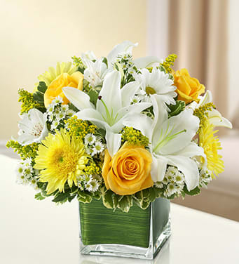BN95414 - Healing Tears - Yellow and White Send a bright and beautiful message of your care and concern. This graceful yellow and white arrangement of roses, lilies, cremones, alstroemeria, daisy poms and solidago is hand-arranged in a cube vase to express your peaceful gesture of sympathy.
