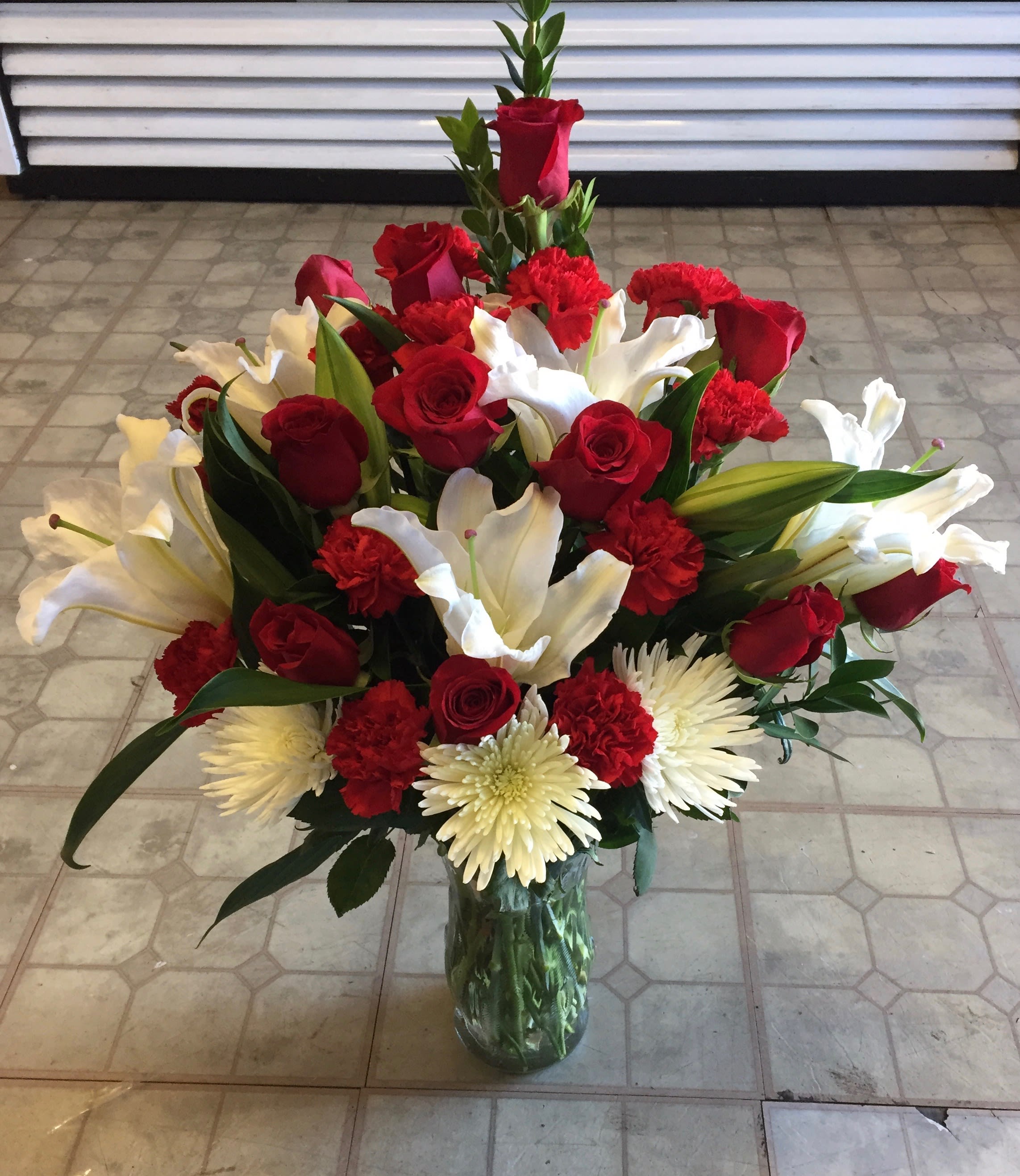 CF3002 - Winter Wonderland Spread holiday cheer with this lavish assortment of red roses, red carnations, white lilies, white spider mums, and foliage artfully arranged in an elegant glass vase. 