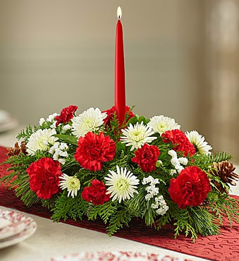 BN90669S - Traditional Christmas Centerpiece (S) Every family has its own holiday traditions, and our classic Christmas centerpiece could be one of yours! Beautifully arranged using fresh, crisp blooms in the signature colors of the season—white lilies, red roses and more—our original display is accented with a fragrant mix of evergreens and pinecones. And for a finishing touch, our florists add a red taper candle, creating a warm and festive glow for all your celebrations!