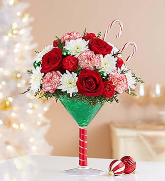 Martini Bouquet Peppermint - Stir up some merry good times with our truly original cocktail arrangement! Fresh roses and carnations are gathered with a festive mix of Christmas greens, green ornament balls and real candy canes for a sweet surprise! Inspired by a cool holiday cocktail, it's gathered in an oversized martini glass to serve up smiles for every holiday celebration. After the holidays, the food-safe container can be used to hold anything from soaps to nuts.
