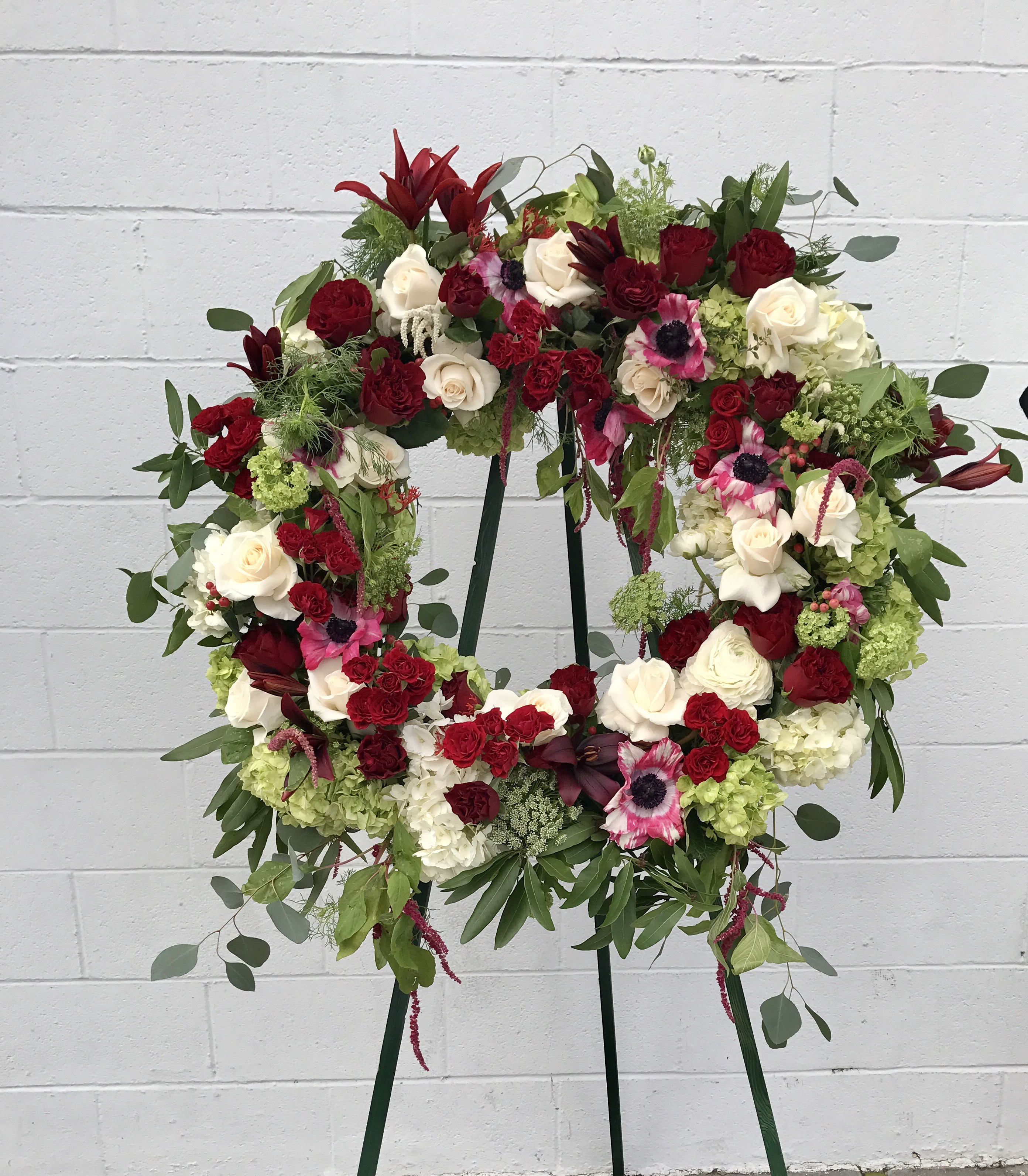 Hold On - A collection of all seasonal flowers and a hint of greenery designed on a large cylinder wreath.  Please let us know what color scheme you wish for based on the style and personality of your loved one.  It's designed on a stand and we can deliver to the location per the timeframe you request. 