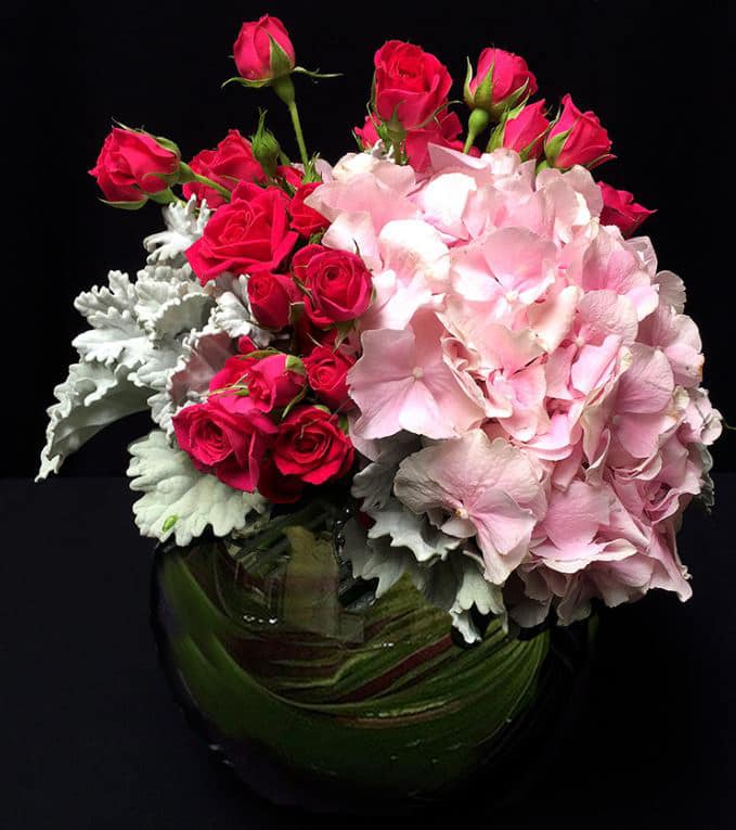 Pink Spring E15-1 - This amazing mix of pink or white hydrangea and deep pink spray roses is perfectly arranged in a ti-leaf lined bubble bowl.