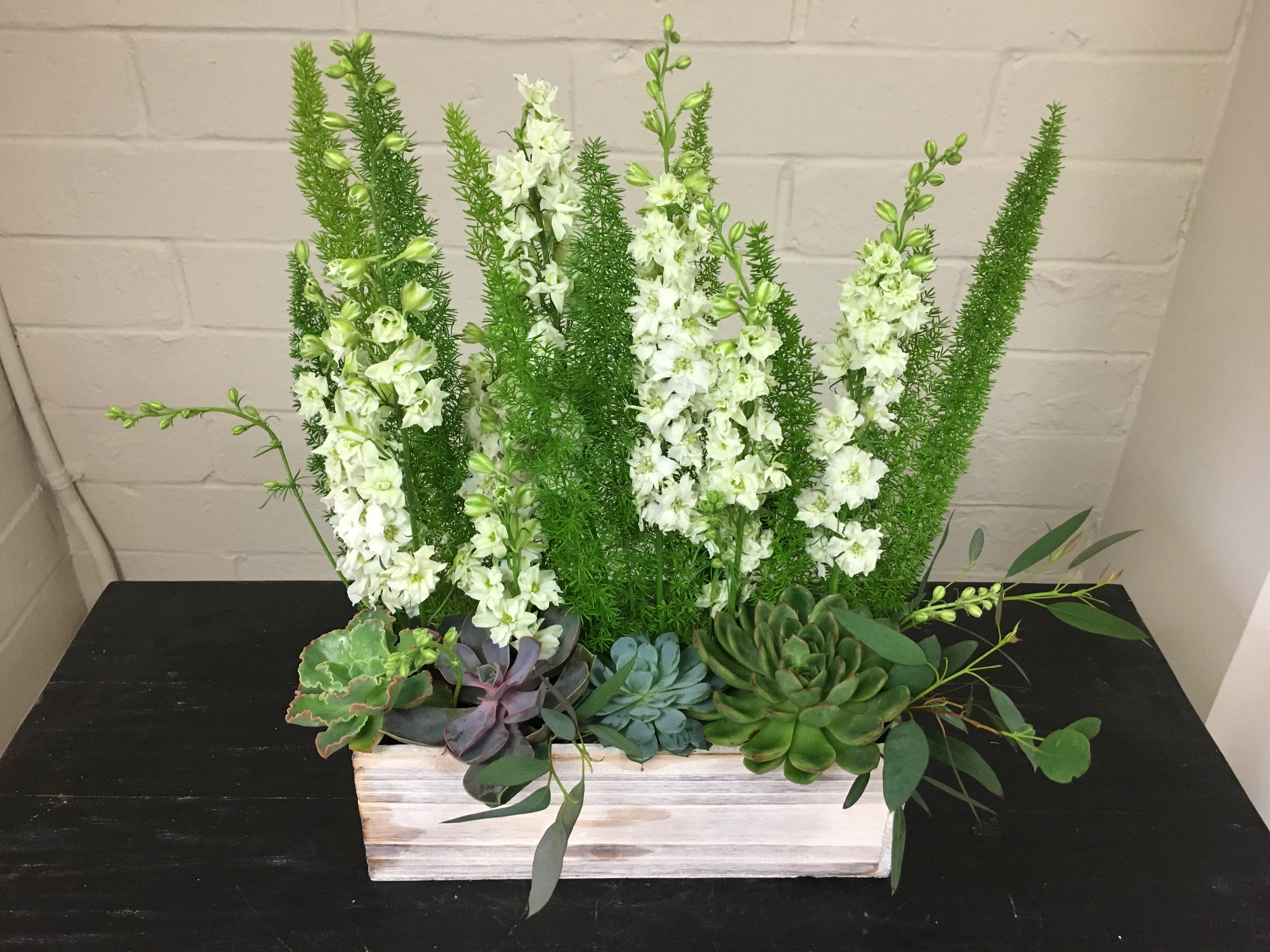 Desert Oasis - Approx Dimension:  12L x 4W x 18H  Lush green arrangement with Succulents, Fox Tails, Delphinium and Eucalyptus leaves in a wooden crate box.  