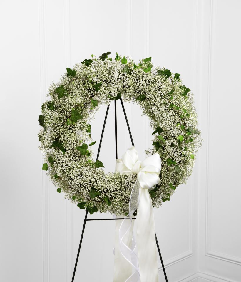 FTD Precious Wreath - The FTD Precious Wreath is a beautiful arrangement to commemorate   their life with sweet sophistication. Stems of baby's breath and ivy   vines are artfully arranged in the shape of a wreath and accented with a   white satin and white sheer bordered ribbon to create a beautiful   presentation for their final farewell service. Displayed on a wire   easel.    no dimensions
