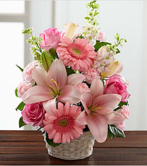 The FTD® Whispering Love™ Arrangement - This fresh, pink bouquet makes a perfect tribute to honor a special someone who, friends, colleagues and family remember as &quot;simply sweet.&quot; This understated tribute handcrafted by an FTD artisan florist is a lovely pink arrangement of roses, larkspur, carnations, gerbera daisies and Asiatic lilies beautifully accented with vibrant greens in a white basket. It brings a touch of color and beauty for a wake, funeral service or to console family or friends at home. Your purchase includes a complimentary personalized gift message. 