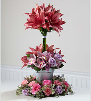 The FTD® Towering Beauty™ Arrangement - When celebrating a life lived with fashion and flair, this vibrant arrangement is an inspired tribute. Its &quot;tiers of joy&quot; are sure to spark happy memories of the departed−perfect for consoling grieving family and friends. Handcrafted by a local FTD artisan florist it is constructed of three levels of blooming color from the ring of striking color at the base, to the dramatic flourish of lilies at the top. It includes lavender and hot pink roses, pink carnations, statice and cymbidium orchids, white waxflower and complemented with lovely, lush greens. A welcome choice for a wake or for a funeral service that will never be forgotten.  Your purchase includes a complimentary personalized gift message.