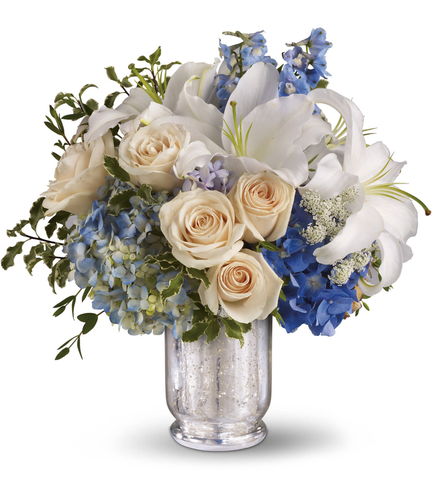 Teleflora's Seaside Centerpiece - Two shades of blue hydrangea are mixed with crème roses, light blue delphinium, fragrant white oriental lilies, delicate Queen Anne's lace, parvifolia eucalyptus and green pitta negra in a beautiful Mercury Glass Antique Hurricane. Approximately 14 3/4&quot; W x 14 3/4&quot; H