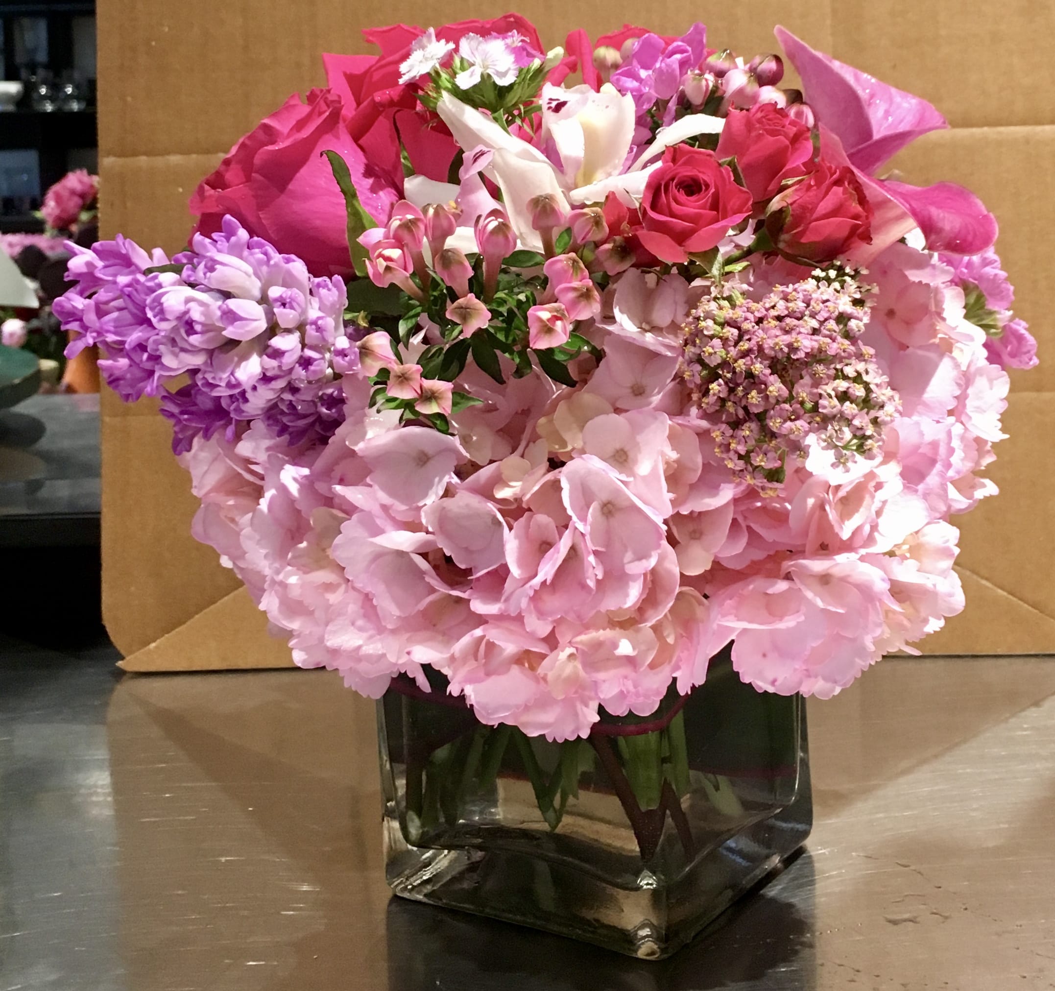 Pastel Nosegay Pastel Nosegay - Custom nosegay style arrangement of pale pink hydrangea, pink roses, lavender calla lilies, pink spray roses, scabiosa, Sweet William, white cymbidium orchids & blue hyacinths in clear glass cube.