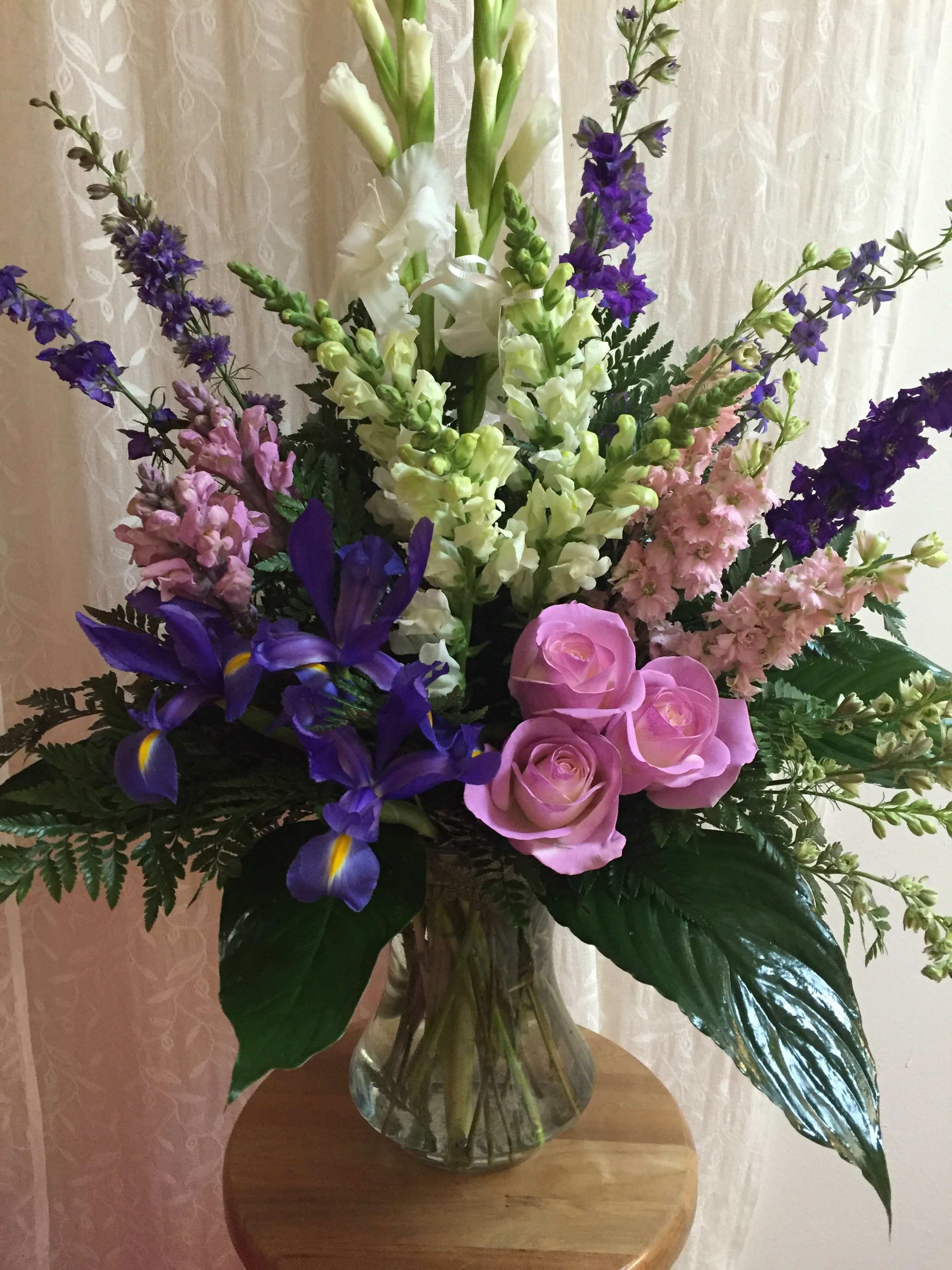 Grand Remembrance Grand Remembrance - Elegant arrangement of jewel toned roses, iris. gladiolus, and stock in a clear glass vase.