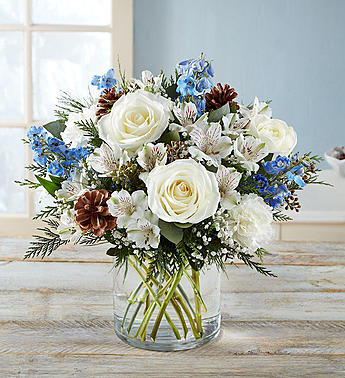 Winter Wishes Bouquet Winter Wishes Bouquet - All-around arrangement with white roses, carnations and Peruvian lilies (alstroemeria); blue delphinium; baby’s breath; seeded eucalyptus and assorted greenery and pinecones Peruvian lilies may arrive in bud form and will open to full beauty in 2-3 days Artistically designed a clear glass cylinder vase