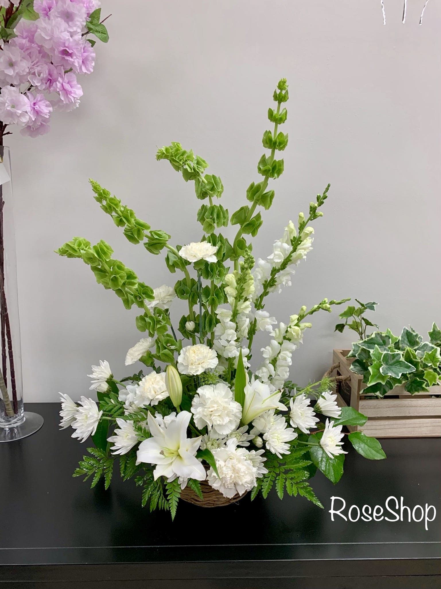 All-white flowers in a basket - A beautiful display of all white flowers- accented with a soft green from bells of Ireland. 