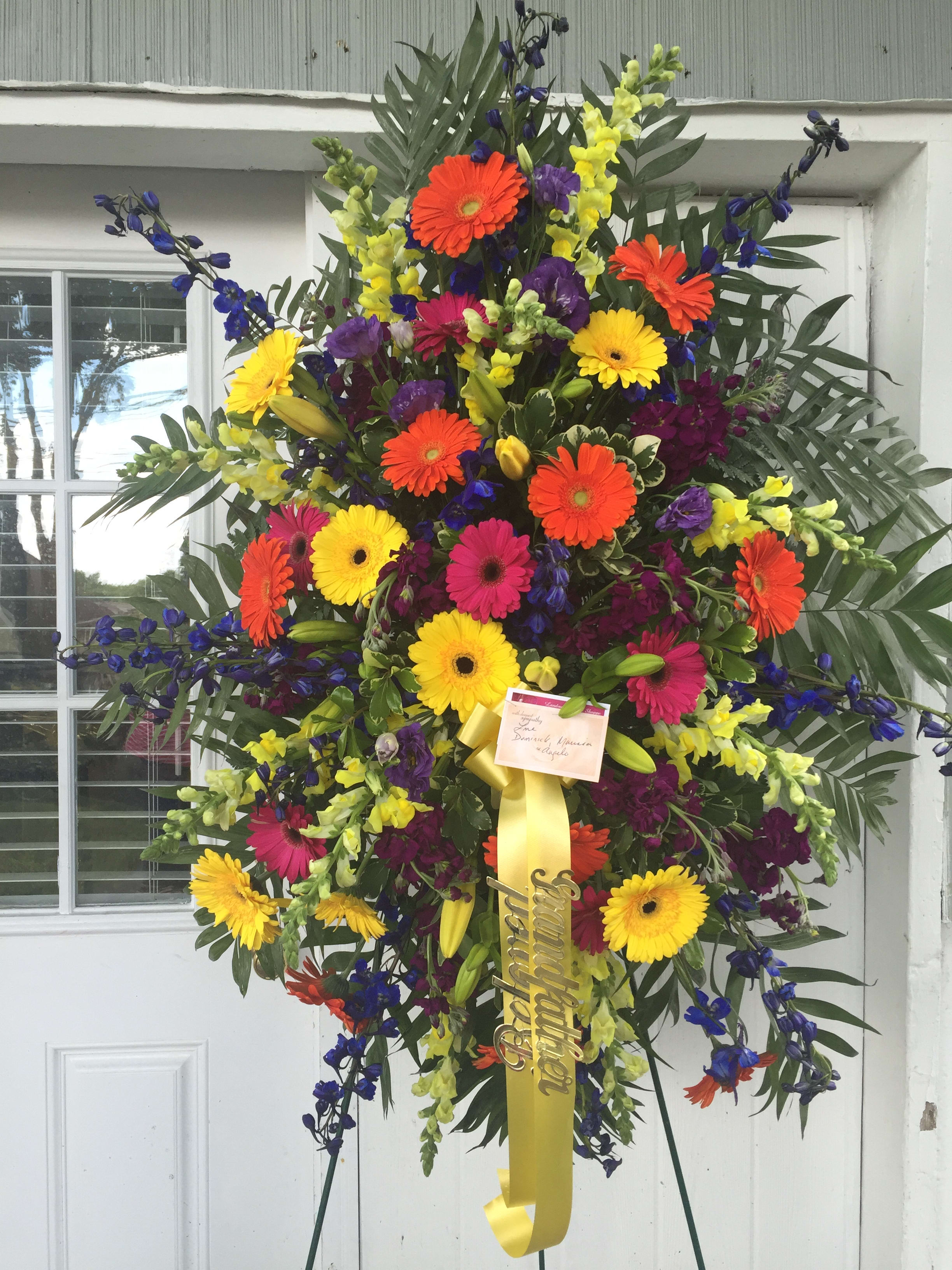 Standing Spray Colorful Blends  - Yellow gerbera daisies, orange gerbera daisies, hot pink gerbera daisies, yellow snap dragon, dark blue delphinium, dark purple lisianthus, premium greens. 