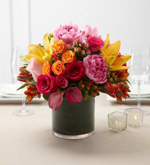 Color Mix Arrangement - The FTD&reg; Color Mix&trade; Arrangement is a bright and beautiful centerpiece set to bring color and life to your wedding reception. Fuchsia roses light pink roses orange parrot tulips hot pink mini calla lilies orange LA Hybrid Lilies orange spray roses and hot pink spray roses are gorgeously arranged in a clear glass cylindrical vase showcasing ti leaves around the stems to give it a fresh and alluring look.