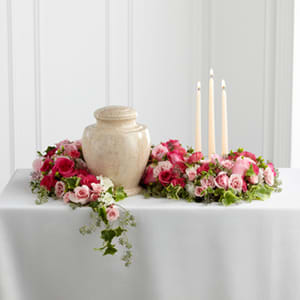 The FTD Remembrance Arrangement - The FTD® Remembrance® Arrangement is a sweetly sophisticated way to display their urn at their final farewell service. Fuchsia and pale pink roses and spray roses are accented with lush greens to form an exquisite arrangement that winds around the base of the urn and curls around 3 ivory taper candles, creating a warm and comforting presentation that commemorates a life that brought kindness and beauty in to the lives of others.
