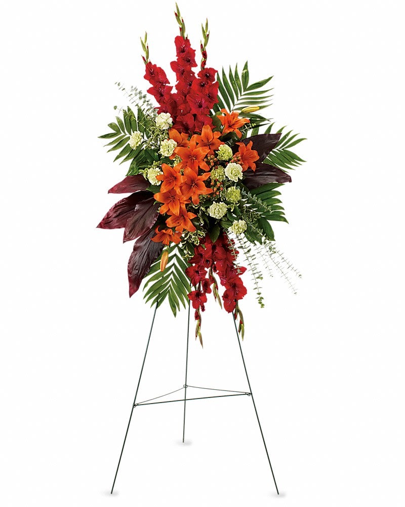 A New Sunrise Spray - When a loved one has passed, this radiant spray of red and orange flowers will be a reminder of happy times past that will never be forgotten. The stunning arrangement includes orange Asiatic lilies, red gladioli, green carnations, peach hypericum, emerald palm and red ti leaves, accented with assorted greenery.