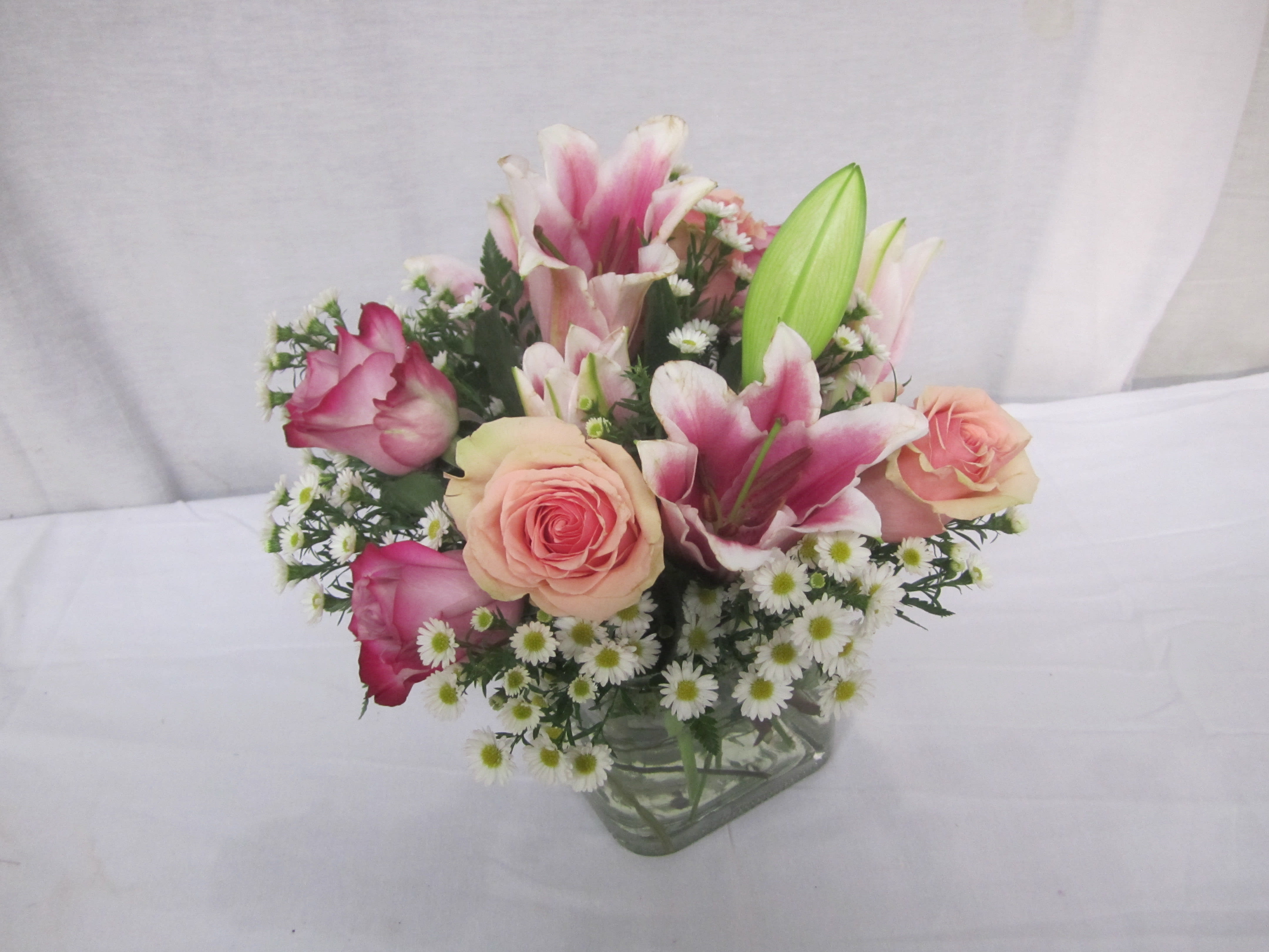 Subtle Sweetness - Harmonious colors delight the eyes, and sweet fragrance fills the air with this elegant composition of peach and pink tones of roses and lilies.  Attractive white aster surrounds the blossoms with softness. The graceful petals will elevate the senses with the calming beauty it bestows.