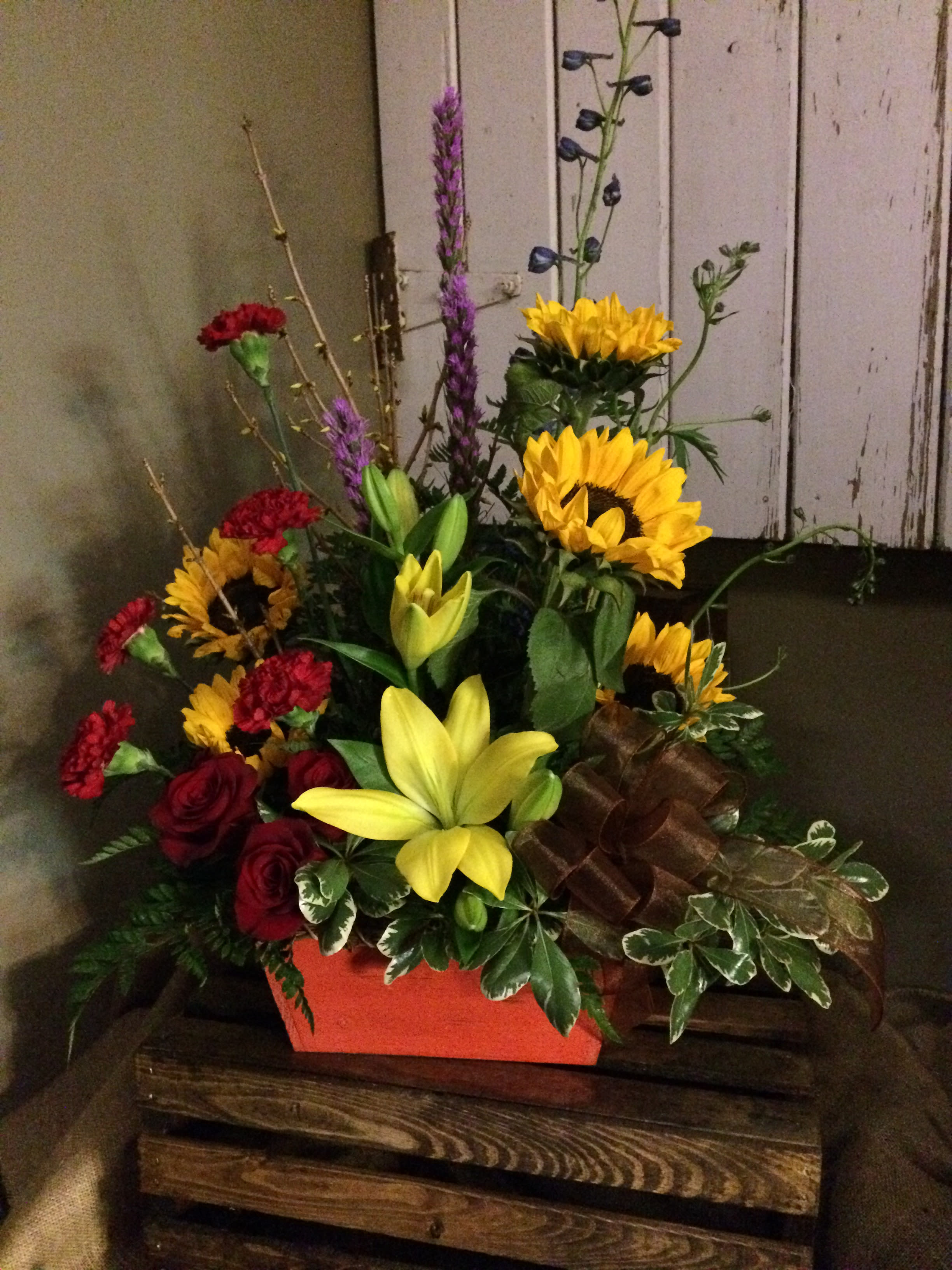 Sunflower Sunset Custom Design by Cold Spring Floral Sunflower Sunset Custom Design by Cold Spring Floral - Sunflower Sunset make a beautiful statement with fresh yellow sunflowers, red roses, purple liatris, blue delphinium and yellow lilies. Natural twigs add to the background while the unique container supports this Sunset inspired arrangement with fresh mixed greenery. Exact flowers and container used are subject to substitutions based on availability.