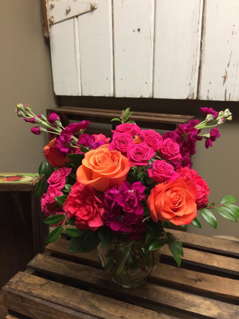 Summer Sunset - This arrangement has orange Roses, purple stock, hot pink spray roses, hot pink Carnations and lush greens.