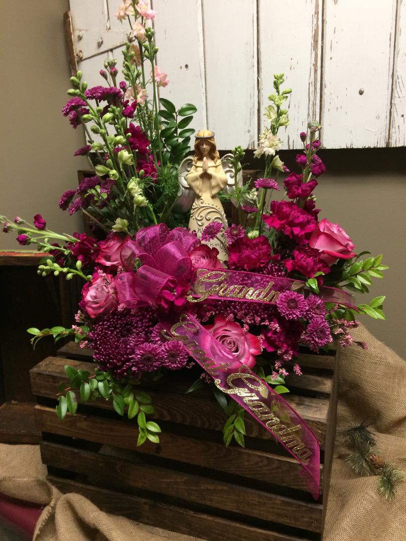 Peaceful Garden - This arrangement includes a beautiful angel surrounded in a garden of pink roses, plum button mums, pink and white larkspur, plum Fuji mums, purple stock, dark pink carnations, and lush greens