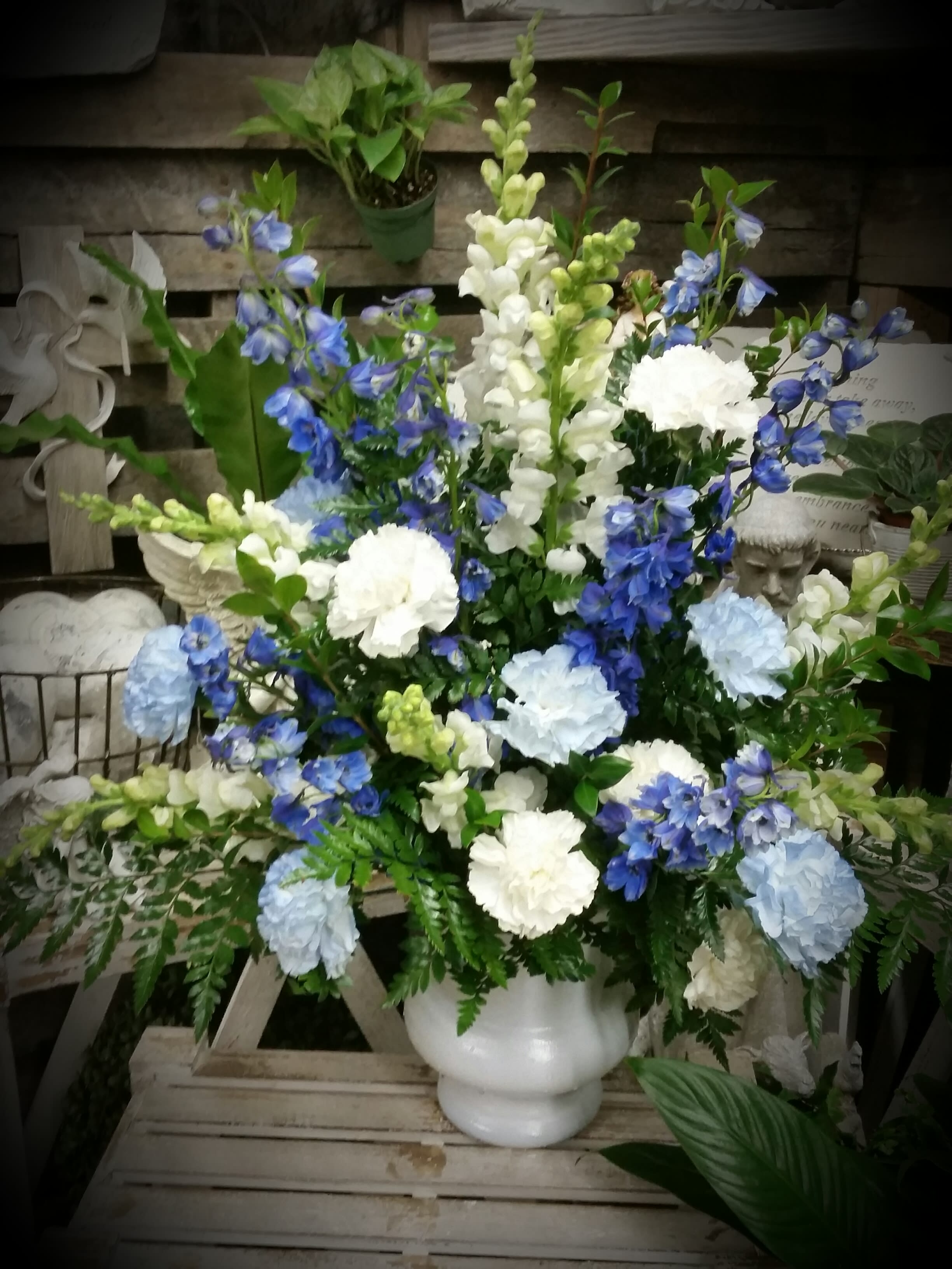 Shades of Blue designed by The Potted Plant - White snapdragons and blue delphinium rise above a field of blue and white carnations with mixes greens fern and myrtle. 