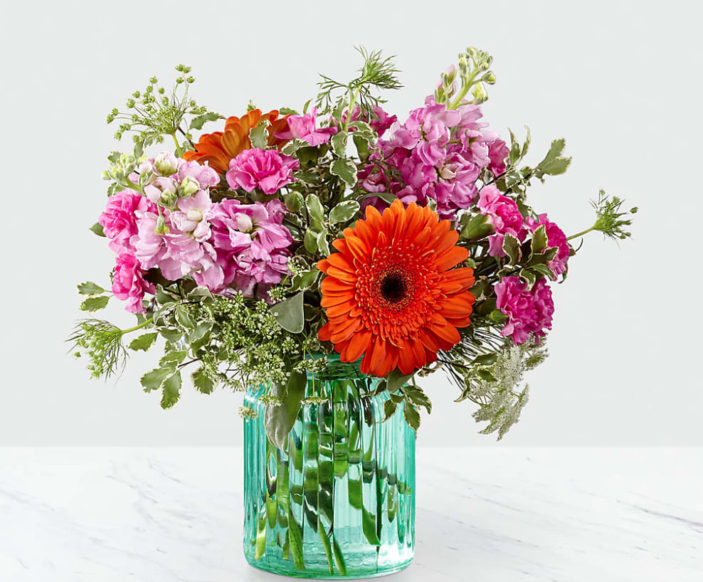 The FTD Aqua Escape The FTD Aqua Escape - FTD® proudly presents the Aqua Escape™ Bouquet. A bold mix of color your special recipient will never forget this simply stunning fresh flower bouquet is ready to make that perfect impression. Bringing together brilliant orange gerbera daisies orange spray roses fragrant pink gilly flower and lavender mini carnations accented with fronds of Queen Anne's Lace and lush greens this flower arrangement is a memory maker. Presented in an aqua colored glass vase to give it a beachy summertime feel this flower bouquet is ready to create a wonderful thank you thinking of you or happy birthday gift. GOOD bouquet is approx. 13"H x 12"W. BETTER bouquet is approx. 14"H x 13"W. BEST bouquet is approx. 15"H x 14"W.