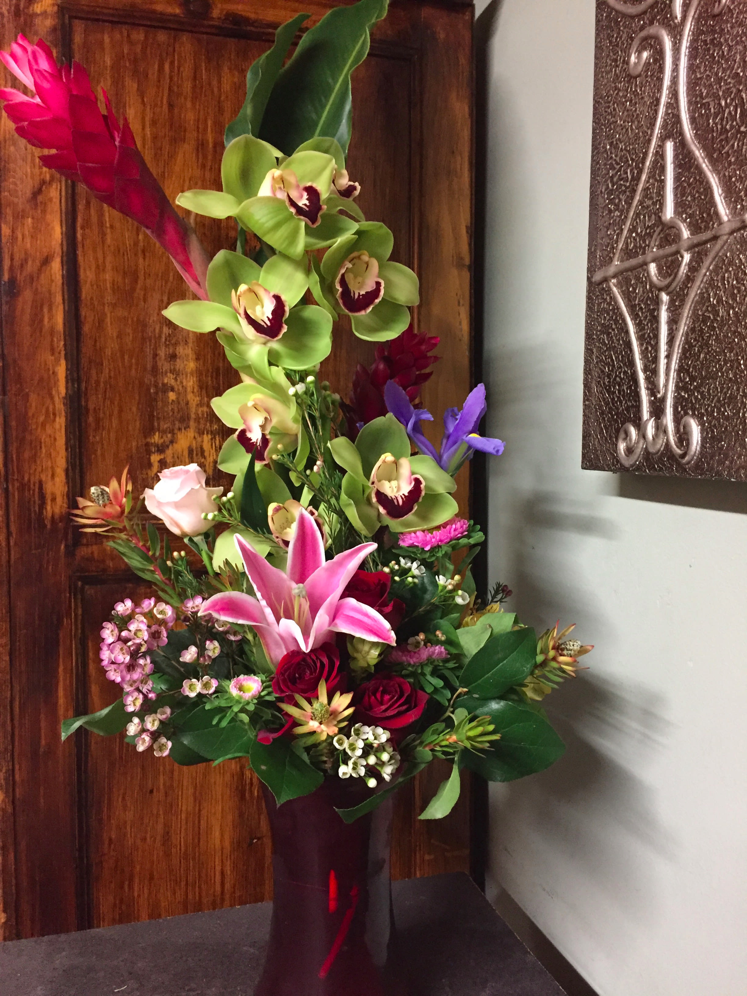 Extravagant Tropical Extravagant Tropical - Cymbidium Orchids, Red Ginger, Lilies, Iris, Proteas, Roses. Arranged in clear glass vase.