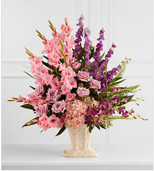 The FTD® Flowing Garden™ Arrangement The FTD® Flowing Garden™ Arrangement - The FTD® Flowing Garden™ Arrangement bursts with a bounty of blooms to create a stunning tribute of the deceased at their final farewell service. Lavender roses, pink gladiolus, purple dendrobium orchids, purple larkspur and pink hydrangea are accented with an assortement of lush, vibrant greens and perfectly arranged in a papier mache urn to create a presentation of grand beauty that symbolizes the life of the departed. GOOD arrangement includes 27 stems. Approximately 34"H x 31"H. Your purchase includes a complimentary personalized gift message.