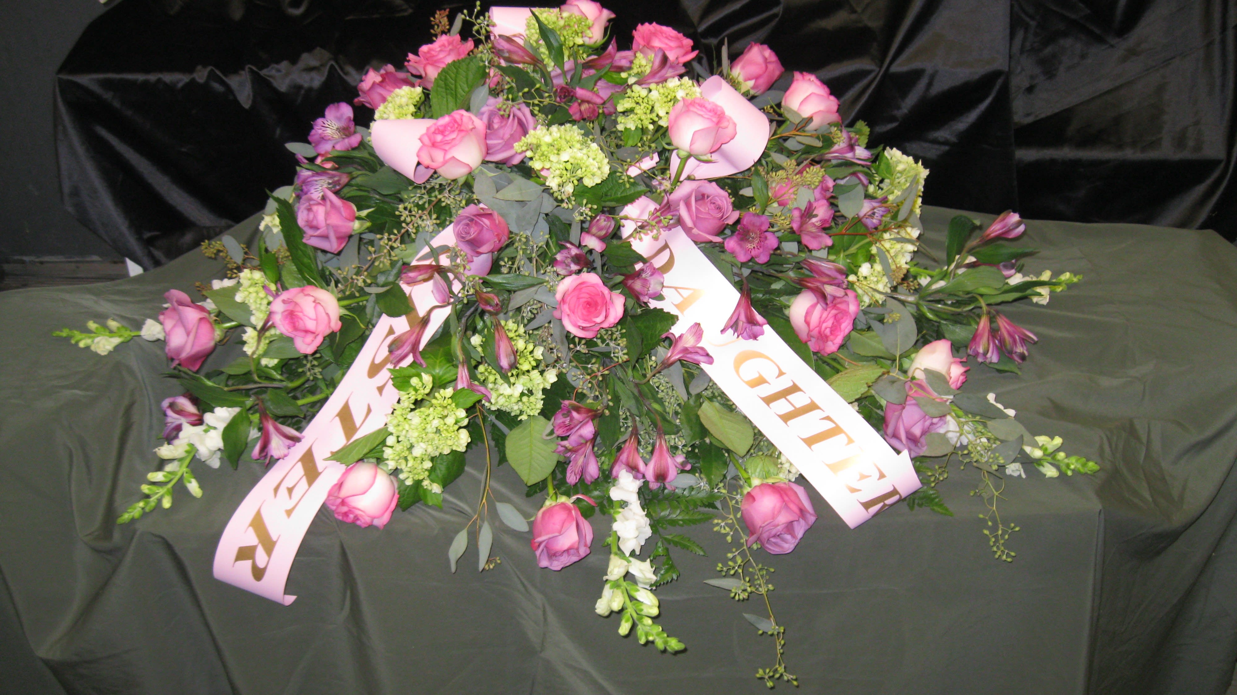 Our Loveliness Casket Cover Our Loveliness Casket Cover - Our Loveliness Casket Cover is beautifully arranged with pink and lavender roses, green hydrangea, pink alstroemeria, white snapdragons and accented with seeded eucalyptus and greens. Ribbons have been added that reflect the relationship of the loved one. Colors and flowers can be changed to your desires.