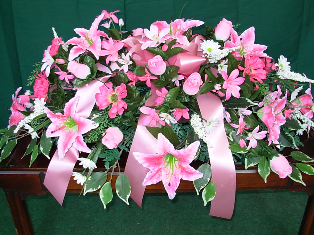 PINK SILK LILLY CASKET SPRAY  NEW-S21 - Our SILK - PERMANENT LILLY CASKET SPRAY  is made of pink stargazer Lilies , soft pink rose buds, pink daisies, white daises with white lupine and is softened with a pink ribbon bow.  Our silk -permanent sympathy flowers are a great economical alternative.  Ideal for your last minute funeral order, silk and permanent flowers are allowed to stay on the grave for months to come by most all cemeteries in our area.. Phone us at 1-800-331-5358 for all your special floral needs and your last minute orders. 