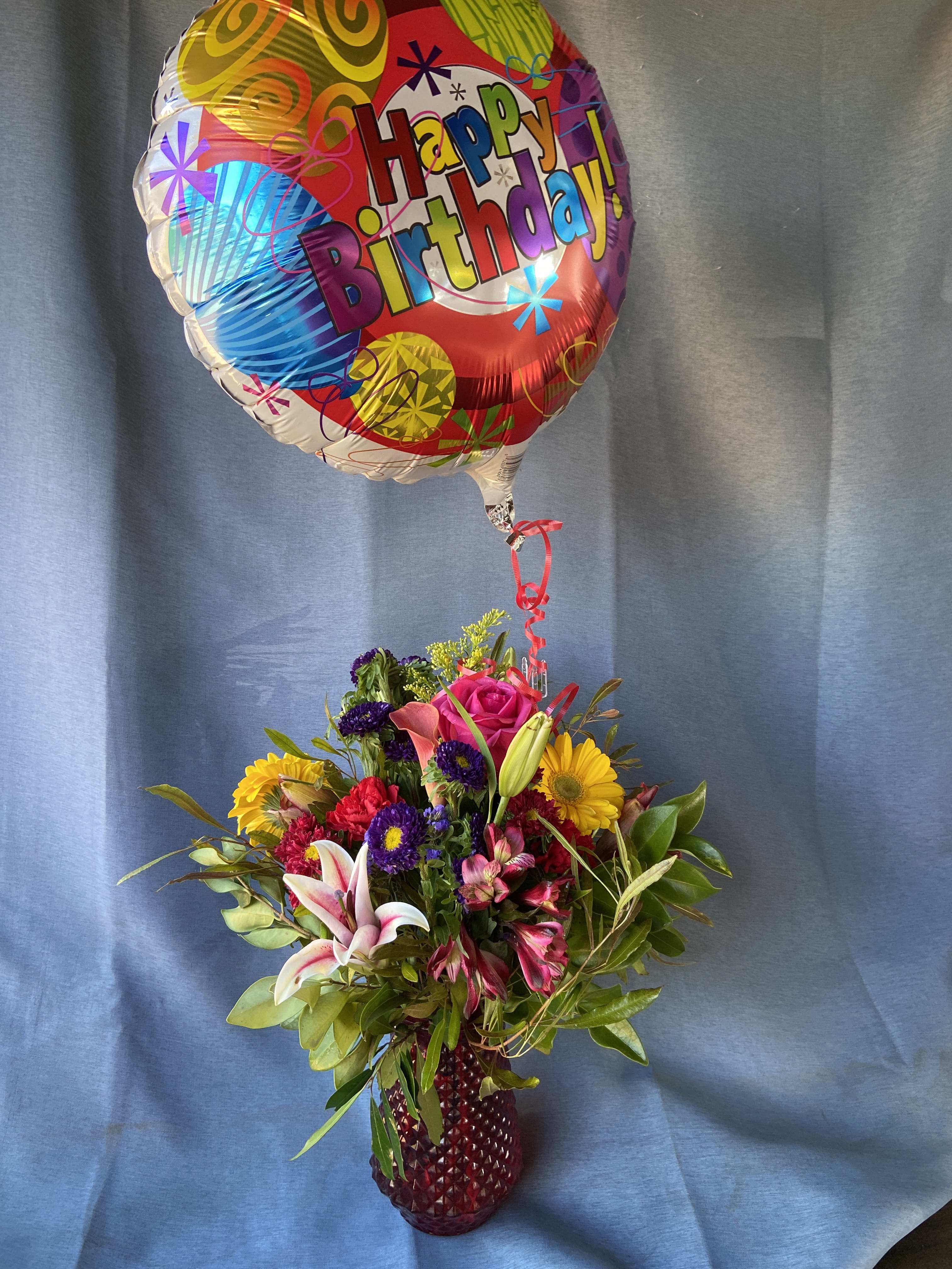 Birthday Celebration - an array of bright colored seasonal flowers in a garden vase and a  balloon to match.