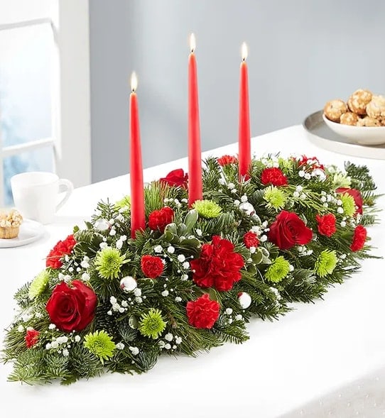 Season's Greetings Centerpiece - Send season’s greetings in classic style. Our charming Christmas centerpiece is hand-arranged with red &amp; green blooms and decorated with delightful ornaments. Tapered candles add to the elegance of this traditional design, sure to bring holiday joy into the hearts and homes of family and friends.