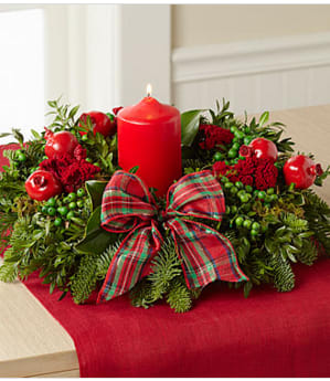 Hearts Aglow Holiday Centerpiece - The Hearts Aglow Holiday Centerpiece brings gorgeous color and light to the holiday table with its rich blooms and lush fragrant greens. A 5-inch red pillar candle is beautifully surrounded by an arrangement of fresh magnolia leaves and flat cedar with golden tips. Perfectly accented with bright red pomegranates and red flax berries, this centerpiece will make a wonderful gift for friends and family or an incredible way to add to the festive beauty of your own home. Candle included. Centerpiece is 13-inches in diameter. Your purchase includes a complimentary personalized gift message.