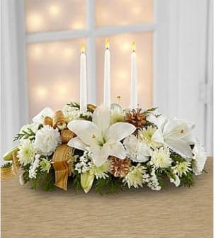 The Seasons Glow™ - The Season's Glow™ Centerpiece by FTD® blooms with winter elegance and holiday enchantment to grace your Christmas celebrations. White LA hybrid lilies, carnations, chrysanthemums and statice are arranged amongst holiday greens and accented with gold pinecones and a gold plaid French wired ribbon for an exquisite look. Arranged to encircle 3 white taper candles, this stunning arrangement will bring a sweet sophistication to your holiday festivities. This centerpiece is approximately 7&quot;H x 21&quot;W. Your purchase includes a complimentary personalized gift message.