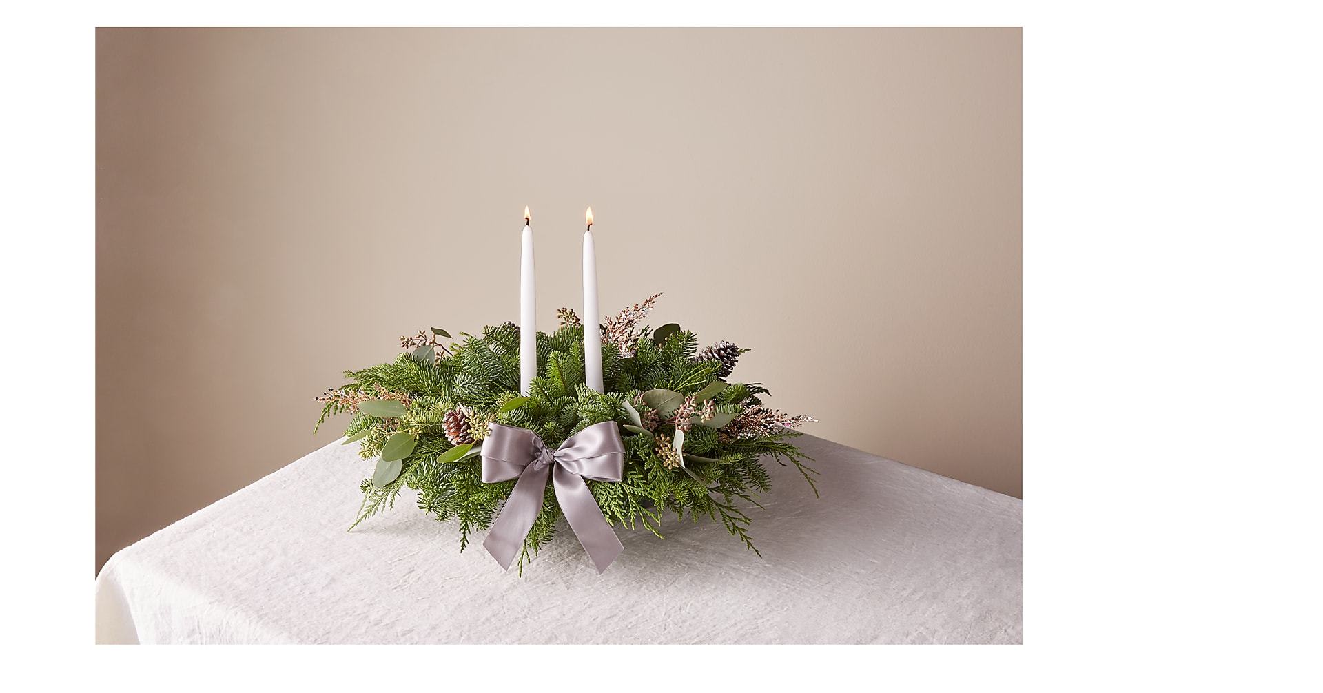 Holiday Centerpiece Holiday Centerpiece - Holiday Centerpiece created with a variety of greens and accented with white candles and frosted pine cones