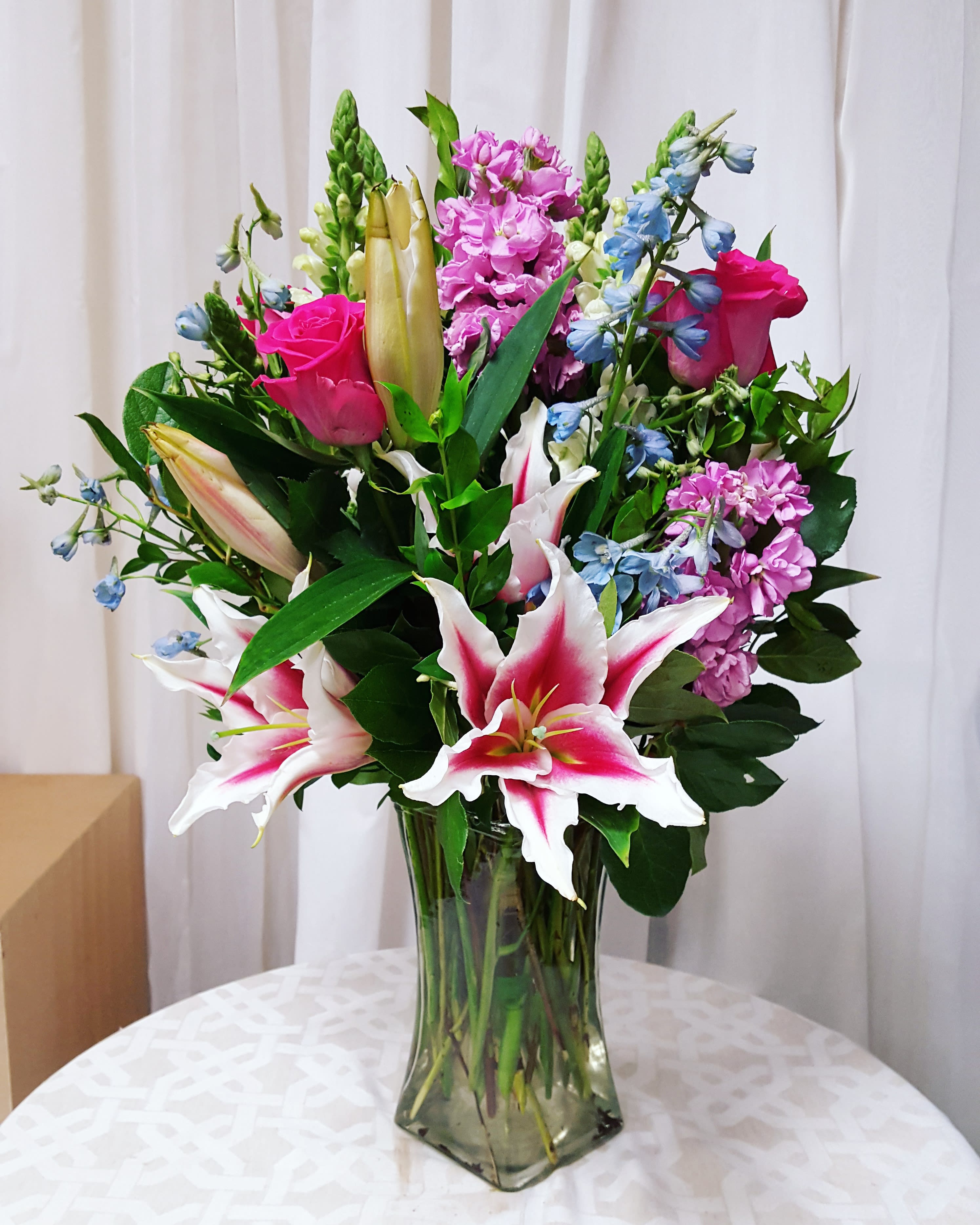 Spring Medley - Bright spring flowers in a tall vase, a go-to classic for every occasion!  Key notes for this design are Stargazer lilies, pink roses, and a tall glass vase. 