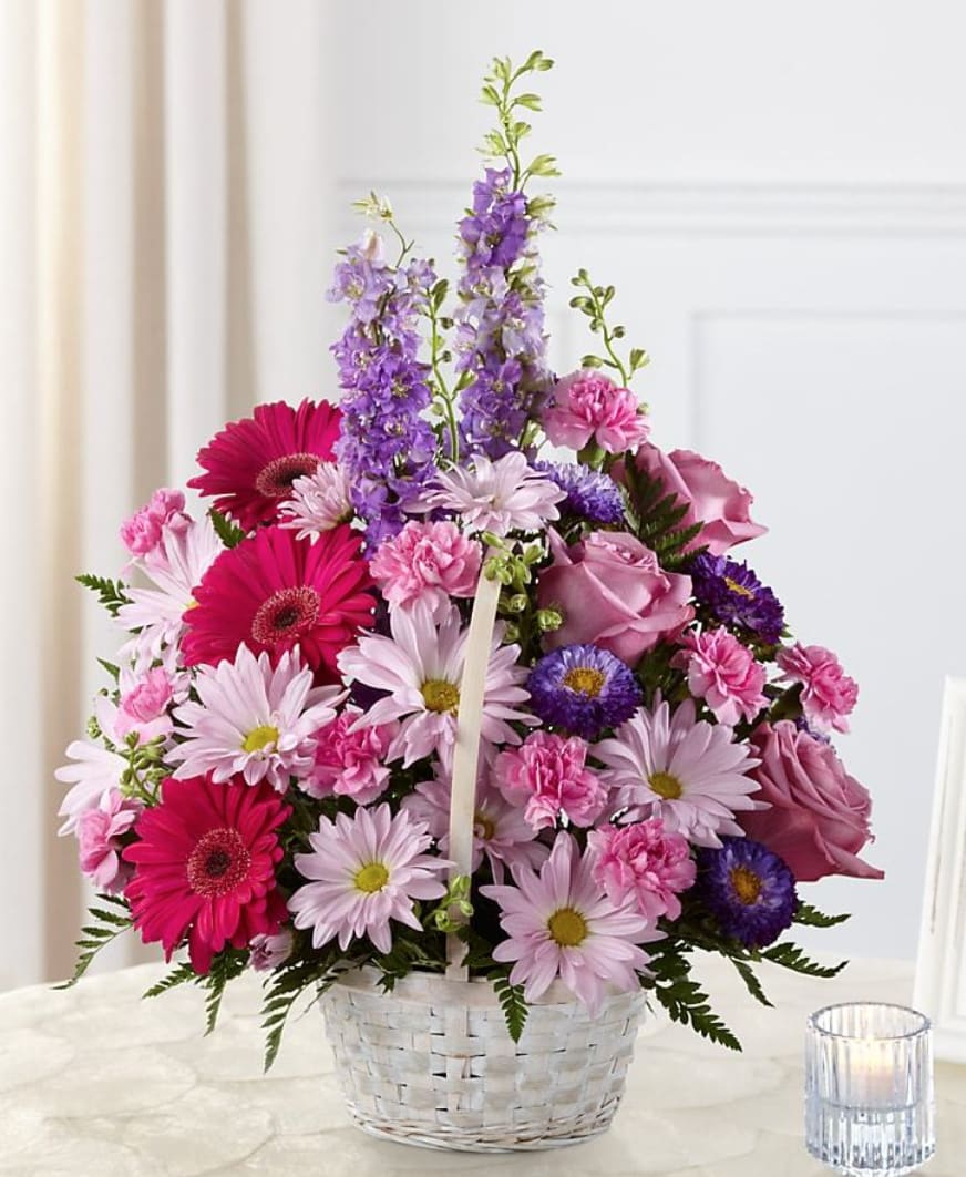 Pastel Peace Basket - A sweet and simple way to offer your condolences. Lavender roses, fuchsia gerbera daisies, lavender daisies, purple larkspur, purple matsumoto asters, pink mini carnations and lush greens are arranged to perfection in a round whitewash handled basket to create a gift that expresses your wishes for sympathy and peace.