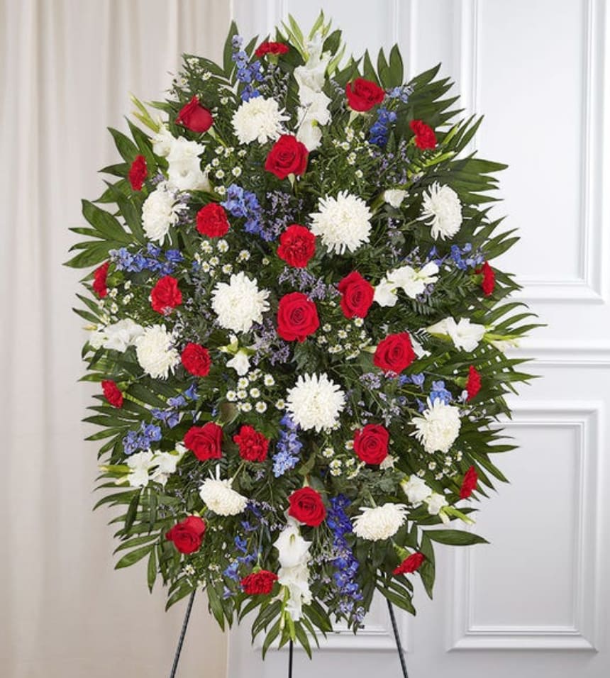 Sympathy Standing Spray: Red, White &amp; Blue  - They served their country with honor and pride, which is how they should be remembered. Our patriotic standing spray arrangement is meticulously handcrafted by our expert florists to honor a brave veteran who has passed away. Filled with fresh blooms in red, white and blue for a lush, full presentation, it’s a proud and fitting final tribute.