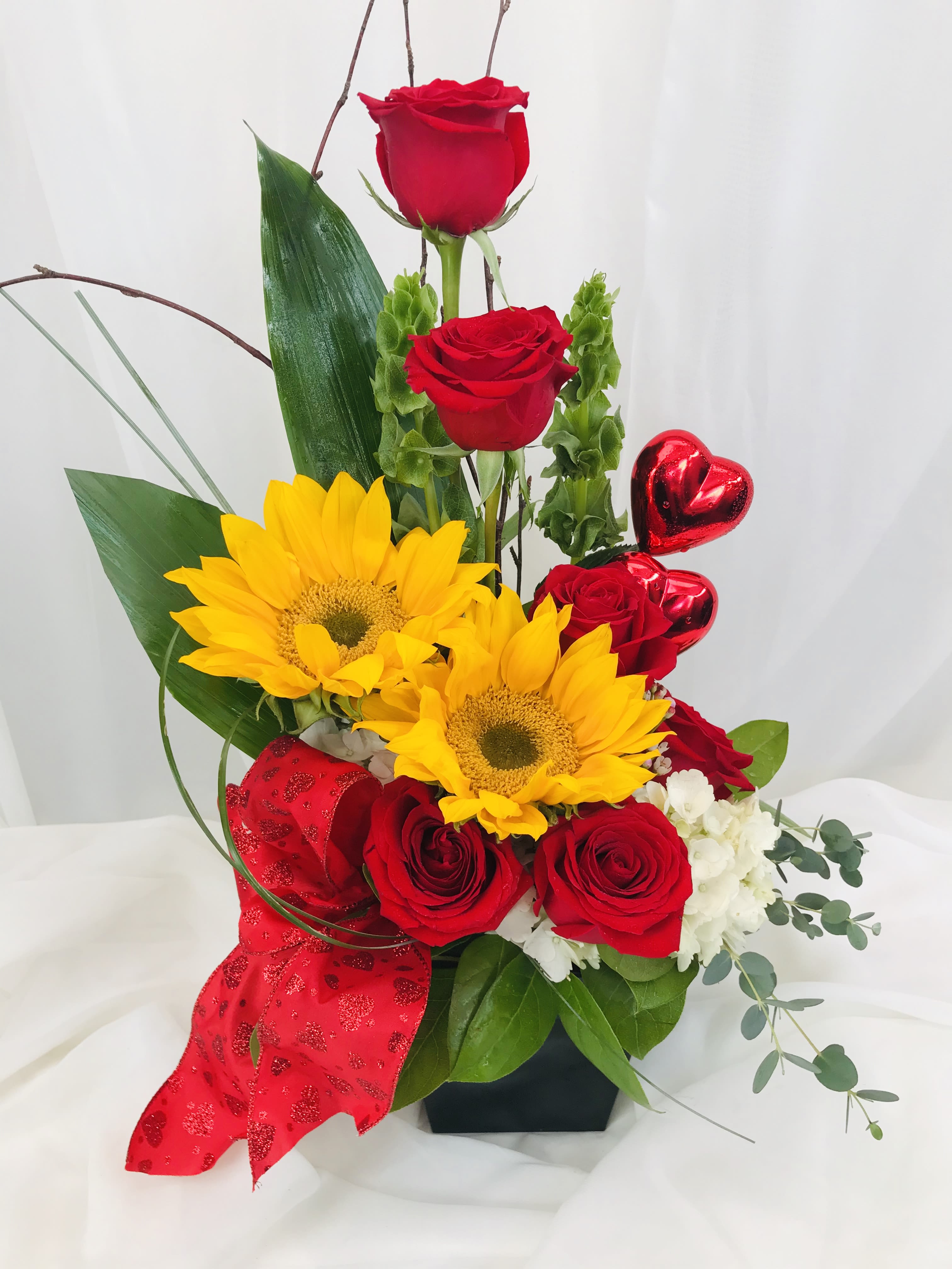Sun Flowers, Roses and Everthing Nice Sun Flowers, Roses and Everthing Nice - This Valentines Day arrangmnet consists of red rose, sunflowers, and is topped off with two heart shaped inclusions and a red bow. The lovely piece is placed in a square black vase.