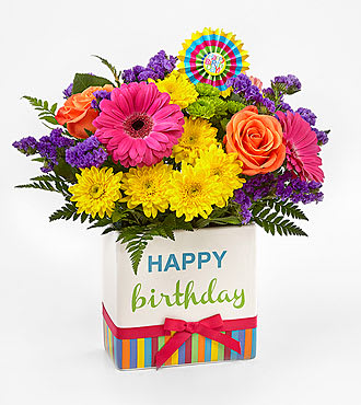 Birthday Brights - The Birthday Brights Bouquet is a true celebration of color and life to surprise and delight your special recipient on their big day! Hot pink gerbera daisies and orange roses take center stage surrounded by purple statice, yellow cushion poms, green button poms, and lush greens to create party perfect birthday display. Presented in a modern rectangular ceramic vase with colorful striping at the bottom, &quot;Happy Birthday&quot; lettering at the top, and a bright pink bow at the center, this unforgettable fresh flower arrangement is then accented with a striped happy birthday pick to create a fun and festive gift
