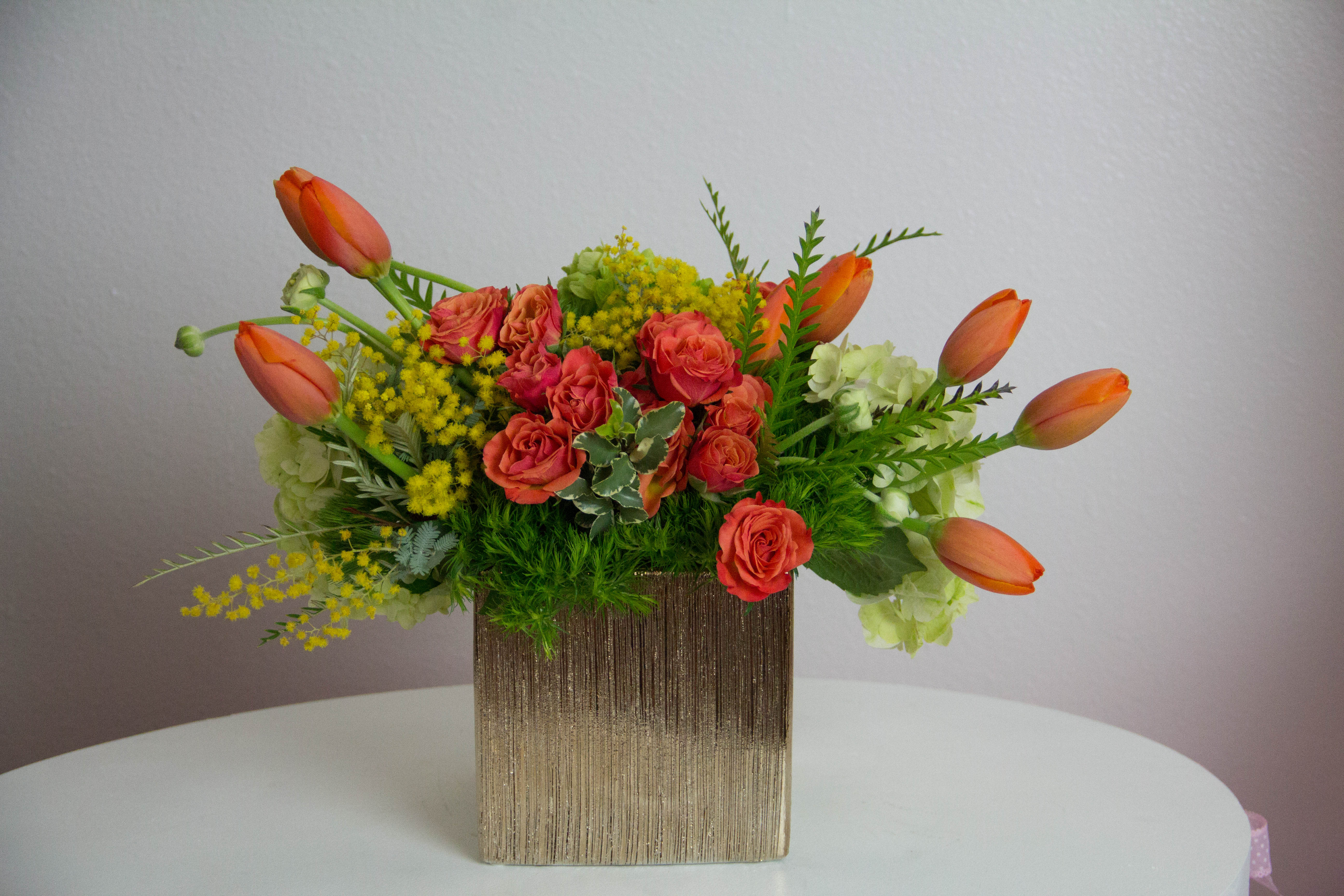 Orange Flame Orange Flame - Green and orange seasonal flowers arranged with yellow filler flowers in a gold ceramic vase. Charming and beautiful composition for spring.