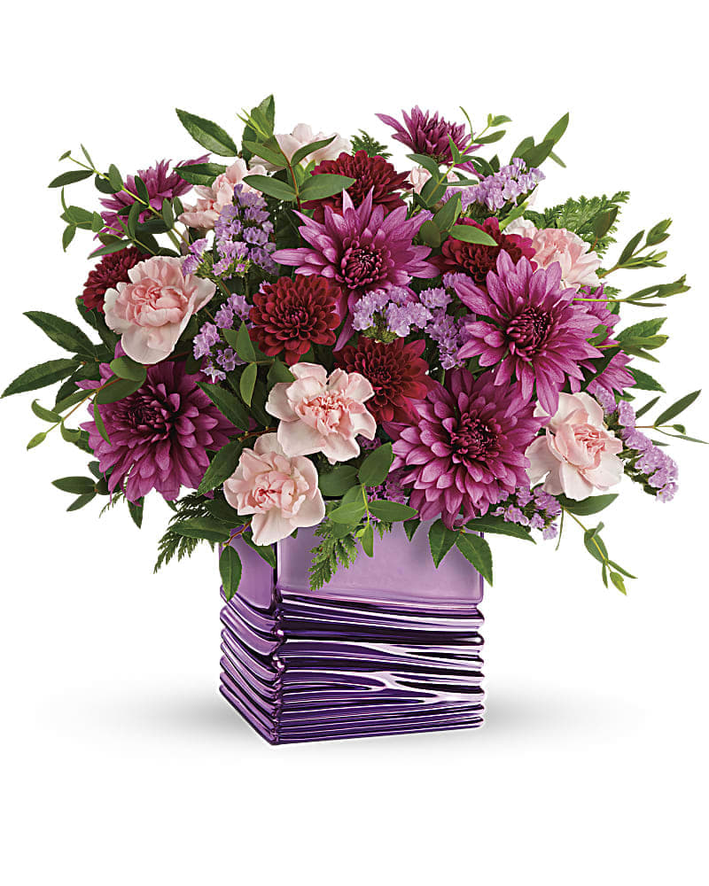 Teleflora's Liquid Lavender Bouquet - Pour on the glam with this luxurious lavender cube! With its shimmering metallic finish and soothing wave detail, it's the perfect complement to a magnificent Mother's Day bouquet of light pink carnations and rich, jewel-toned mums. Light pink miniature carnations, burgundy cushion spray chrysanthemums, purple cushion spray chrysanthemums and lavender sinuata statice are arranged with huckleberry and parvifolia eucalyptus. Delivered in a Liquid Lavender cube.